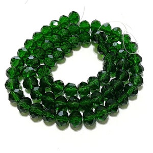May include: Strand of faceted, emerald green beads. The beads are strung on a clear string and have a multi-faceted surface that reflects light. The beads are a deep, rich green color and are arranged in a curved pattern.