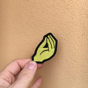 Puede incluir: Parche de hierro bordado amarillo de una mano haciendo el gesto italiano.