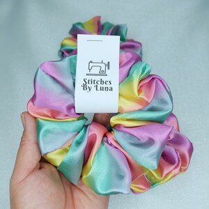 May include: Rainbow ombre satin scrunchie with a white tag that says "Stitches By Luna" and a sewing machine icon.