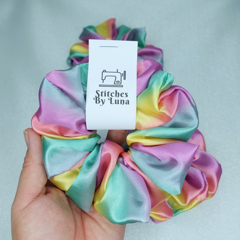 May include: Rainbow ombre satin scrunchie with a white tag that says "Stitches By Luna" and a sewing machine icon.