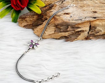 May include: A silver chain bracelet with a flower charm. The flower has purple and white enamel and clear rhinestones.