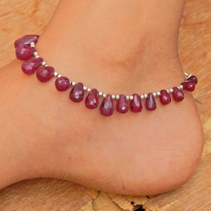 Puede incluir: Un tobillo de plata con cuentas de piedras preciosas rojas. El tobillo está hecho de pequeñas cuentas de plata y cuentas de piedras preciosas rojas que tienen forma de lágrima.