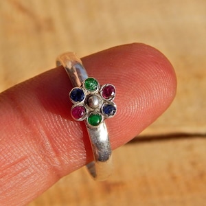 May include: A silver ring with a flower design featuring red, blue, and green gemstones.