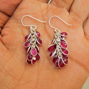 May include: A pair of dangle earrings with a cluster of pink gemstones hanging from a silver chain. The earrings have a hook closure.