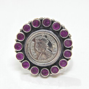 May include: A silver ring with a round coin featuring a profile of Queen Victoria. The coin is surrounded by a circle of purple gemstones.