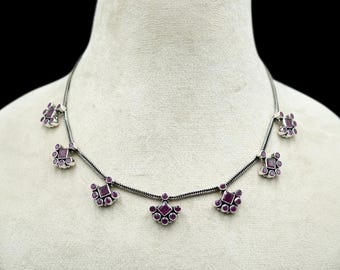 May include: A silver necklace with a delicate chain and multiple pendant charms. Each charm features a cluster of small, round, purple gemstones arranged in a crescent shape.
