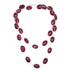 Puede incluir: Un collar de dos hilos con piedras preciosas ovaladas de color rojo intenso engastadas en una cadena de plata. Las piedras están espaciadas uniformemente, creando un efecto de capas. El collar está diseñado para ser usado alrededor del cuello.
