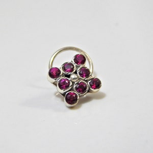 以下が含まれることがあります： 花の形にセットされた8つのピンクの宝石のクラスターが付いたシルバーの鼻のリングです。
