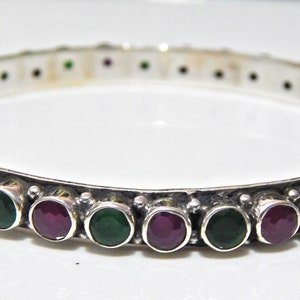 May include: Silver bangle bracelet with alternating green and purple gemstones.
