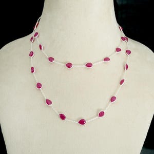 Peut inclure: Un collier en chaîne argent avec des pierres de couleur rouge rubis en forme de goutte. Le collier est superposé et a un design délicat.