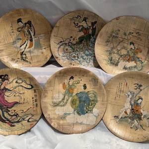 Puede incluir: Seis platos redondos de bambú con escenas pintadas de mujeres con vestimenta tradicional china. Los platos están decorados con diseños intrincados y presentan una variedad de colores, incluyendo dorado, rojo, azul y verde.