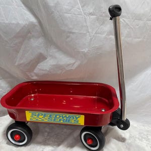 Puede incluir: Un vagón de juguete de metal rojo con neumáticos negros y un asa cromada. El vagón tiene una pegatina amarilla y azul "Speedway Series" en el lateral. Las ruedas tienen llantas blancas y tapacubos rojos.