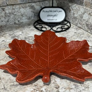 May include: A ceramic leaf-shaped dish in a warm, reddish-brown hue. The dish features detailed veining and a glossy finish. The dish is a decorative piece, perfect for fall or Thanksgiving.