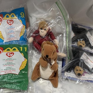 May include: A collection of Ty Beanie Babies in their original packaging. The beanie babies include a red monkey, a brown squirrel, and two black bears. The packaging includes the Ty logo and the name of the beanie baby.