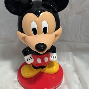 K&ouml;nnte beinhalten: Mickey Mouse-Figur mit schwarzem Kopf und Ohren, hellbraunem Gesicht und roter Basis. Die Figur hat wei&szlig;e Handschuhe, rote Shorts mit wei&szlig;en Kn&ouml;pfen und gelbe Schuhe. Auf der Basis steht "Walt Disney World Resort."