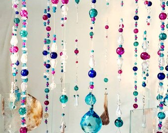 May include: A beaded mobile with strands of turquoise, pink, and blue beads hanging from a white metal frame. The mobile also includes clear crystal beads, a large turquoise crystal, and several clear glass pieces.