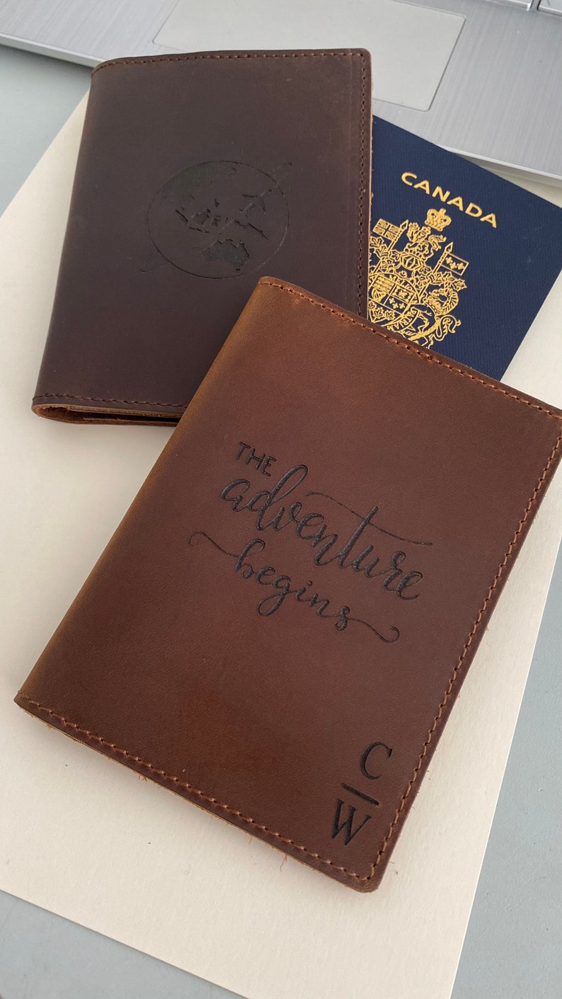 Puede incluir: Dos porta pasaportes de cuero marr&oacute;n. Uno tiene un dise&ntilde;o de globo terr&aacute;queo y el otro tiene el texto "The adventure begins" y las iniciales "C W".