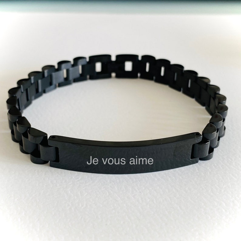 May include: A black stainless steel bracelet with a rectangular tag that reads "Je vous aime".