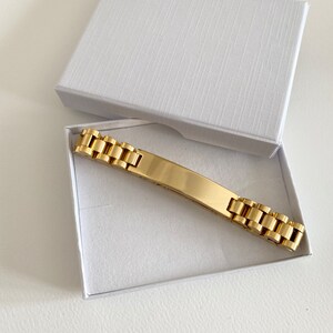 May include: A gold-toned bracelet with a rectangular, flat, blank tag. The bracelet is in a white box.