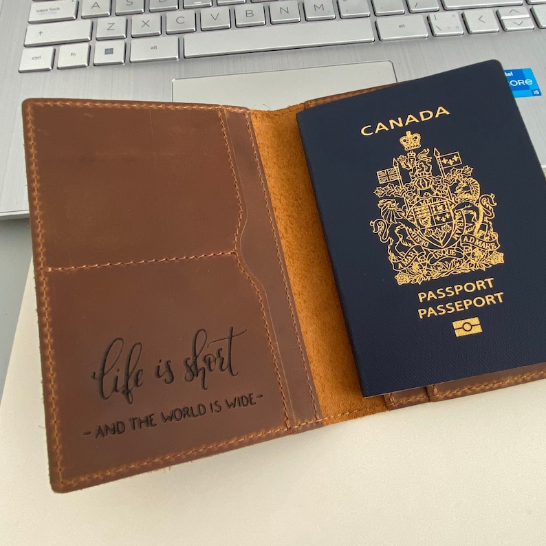 Puede incluir: Un portapasaporte de cuero marr&oacute;n con una cita que dice "la vida es corta - y el mundo es grande" y un pasaporte canadiense en su interior.