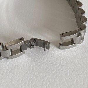 May include: A silver watch band with a clasp that is open. The band is made of metal links.