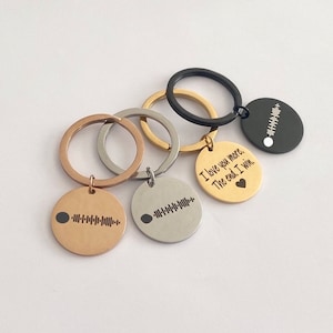 Peut inclure: Trois porte-clés avec des anneaux métalliques de différentes couleurs et des étiquettes rondes. Les étiquettes présentent un motif de code-barres et du texte. Une étiquette indique "I love you more. The end. I win." avec un petit symbole de cœur.