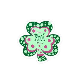 May include: A sticker in the shape of a shamrock with the text "Can't Pinch This." The shamrock has a light green center with pink accents and is surrounded by dark green and small white shamrocks.