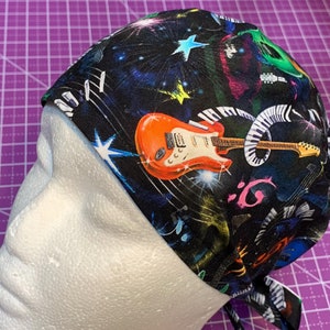 May include: A black scrub hat with a colorful musical print featuring a guitar, piano keys, and musical notes.
