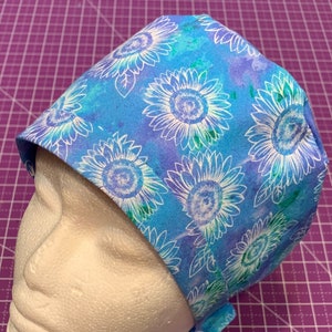 May include: A blue and white patterned surgical scrub hat with a sunflower design. The hat is made of a soft, comfortable fabric and has a tie at the back.