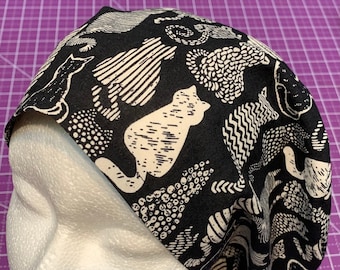 May include: Black scrub hat with a white cat print pattern. The hat is made of a soft, comfortable fabric and is perfect for nurses, doctors, and other healthcare professionals.