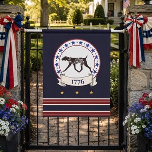 May include: A rectangular navy blue garden flag featuring a central white circle bordered by blue stars, containing a black silhouette of a dog. Below the dog is a white banner with the text 1776, three yellow stars, and horizontal red and white stripes.