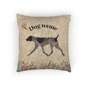 May include: Tan throw pillow featuring a running dog illustration with the text "Dog name" in black. The dog is brown and black, with a black head and a dark patch on its back. The pillow has a textured appearance.