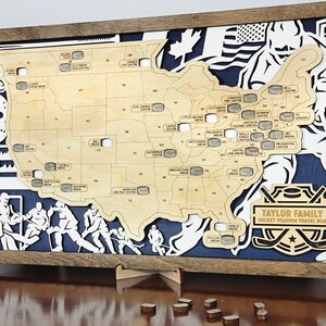 May include: A wooden map of the United States with hockey puck cutouts representing different hockey stadiums. The map is framed in a brown wood frame and has a blue background with hockey stick silhouettes. The text "TAYLOR FAMILY HOCKEY STADIUM TRAVEL MAP" is printed on the map.