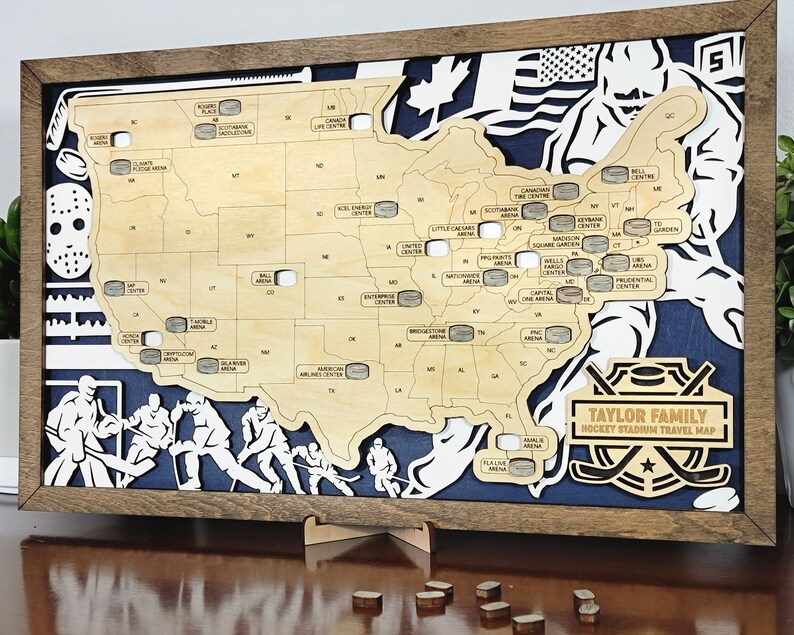 May include: A wooden map of the United States with hockey puck cutouts representing different hockey stadiums. The map is framed in a brown wood frame and has a blue background with hockey stick silhouettes. The text "TAYLOR FAMILY HOCKEY STADIUM TRAVEL MAP" is printed on the map.