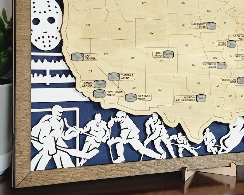 May include: A wooden map of the United States with hockey arenas marked with puck-shaped icons. The map is framed in wood and has a blue background with hockey players cut out of the wood. The map is on a wooden stand.