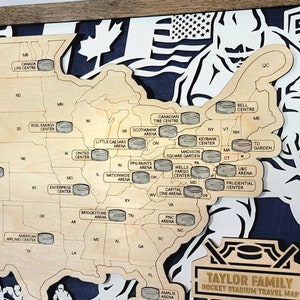 May include: A wooden map of the United States with hockey pucks marking the locations of different hockey arenas. The map is labeled "Taylor Family Hockey Stadium Travel Map".