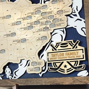 May include: A wooden map of the United States with hockey arenas marked with small circles. The map is framed in a brown wood frame. The text "TAYLOR FAMILY HOCKEY STADIUM TRAVEL MAP" is on the bottom of the map.