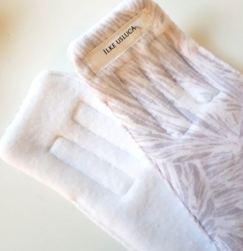 May include: A pair of white fleece gloves with a brown and white patterned design on one glove. The patterned glove has a white label with the text "ILKE USLUGA" on it.