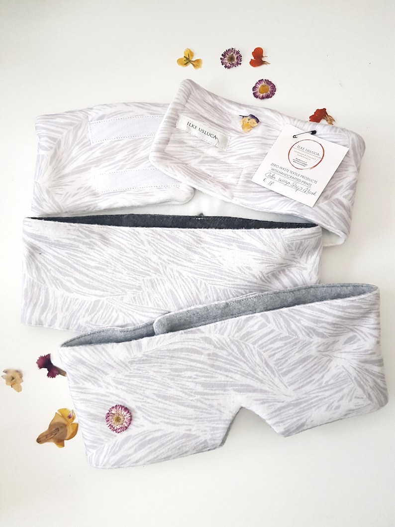 May include: White eye mask with a gray fleece lining and a white and gray zebra print. The eye mask is handmade and has a label that reads "Zero Waste Textile Products, Vienna, handcrafted print, Color: Zebra Grey Print, &euro; 16".