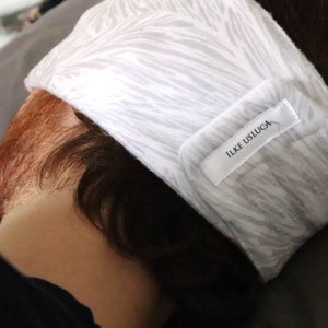 May include: White sleep mask with a gray and white zebra print pattern. The mask has a white label with the text "ILKE USLUCA" on it.