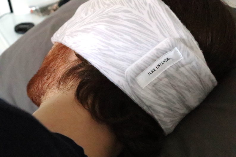 May include: White sleep mask with a gray and white zebra print pattern. The mask has a white label with the text "ILKE USLUCA" on it.