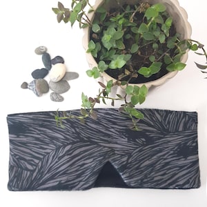 May include: A black and gray sleep mask with a wavy pattern. The mask is made of soft fabric and is designed to block out light.