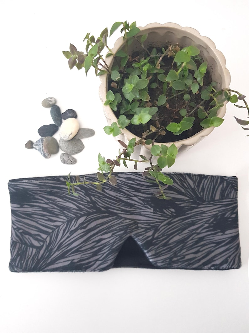 May include: A black and gray sleep mask with a wavy pattern. The mask is made of soft fabric and is designed to block out light.