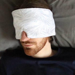 May include: A person wearing a white sleep mask with a leaf pattern on a gray pillow.