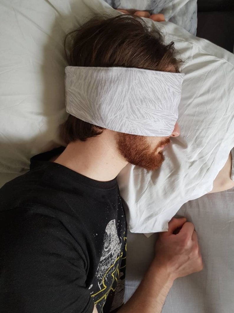May include: A person sleeping in bed with a white and gray patterned sleep mask over their eyes.