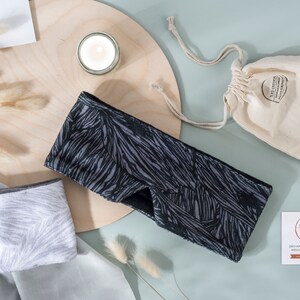 May include: Two black and white patterned sleep masks with a gray sleep mask on a white surface. The sleep masks are made of soft fabric and are designed to block out light. The sleep masks are packaged in a small white drawstring bag. The bag has a label that says "Handcrafted with Love".