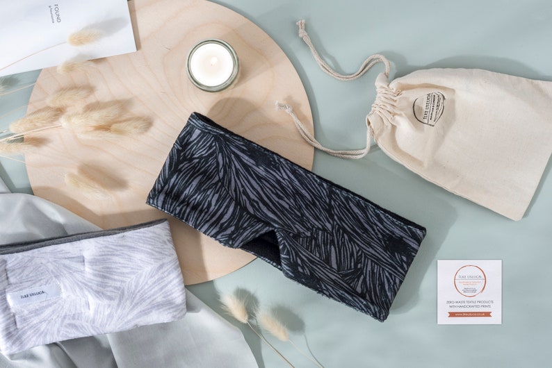 May include: Two black and white patterned sleep masks with a gray sleep mask on a white surface. The sleep masks are made of soft fabric and are designed to block out light. The sleep masks are packaged in a small white drawstring bag. The bag has a label that says "Handcrafted with Love".