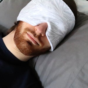 May include: A person wearing a white and gray patterned sleep mask while lying on a gray pillow.