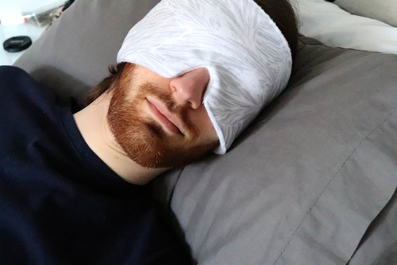 May include: A person wearing a white and gray patterned sleep mask while lying on a gray pillow.