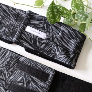 May include: Two black and gray fabric wrist wraps with a black and white leaf pattern. The wrist wraps have adjustable velcro closures. The brand name "Like Usluca" is printed on a white label on one of the wraps.